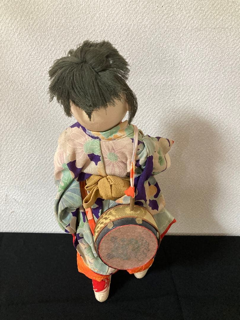 古い縮緬の着物を重ね着、手作りの太鼓を肩からさげています。口に縮緬の椿